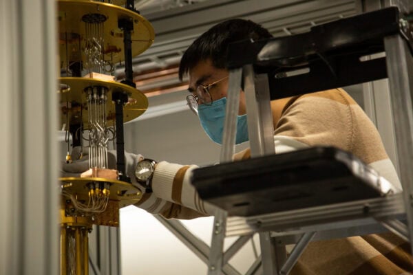A researcher wearing a mask and gloves adjusts the wiring on a dilution refrigerator.
