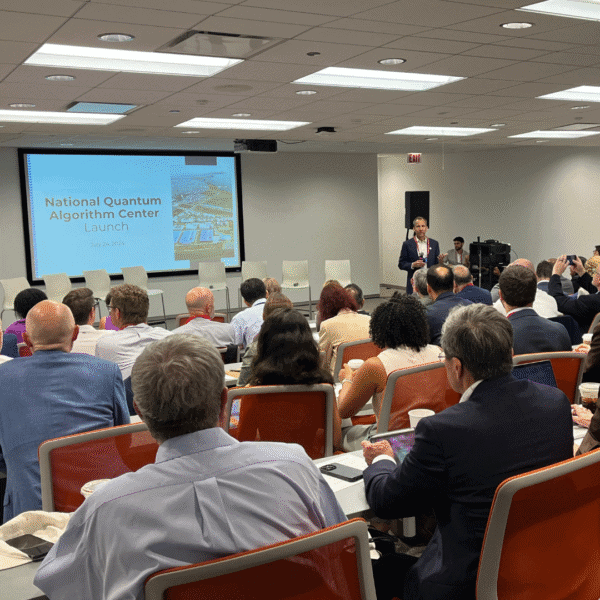 Dr. Harley Johnson presents to a full room during the National Quantum Algorithm Center (NQAC) networking breakfast, with a launch slide displayed behind him and attendees seated attentively with laptops and coffee.