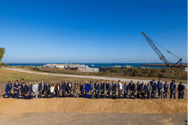 A large group of government, community and industry leaders stands side by side holding shovels for the IQMP groundbreaking ceremony.